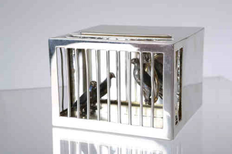 An interesting Edwardian silver bird cage box, WH, London 1906, the rectangular box with hinged cover opening to reveal a gilded interior, fronted by cage with a bird perched on a suspended loop and another on the ground, each bird retaining some enamel p