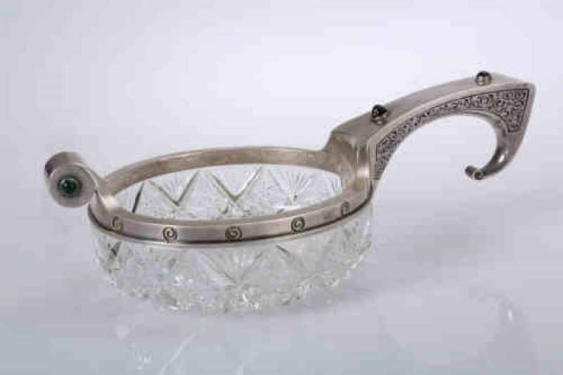 A Russian silver mounted cut glass kovsch, the handle set with two cabochon ''jewels'', the circular mount embellished with a frieze of scrolls, issuing a ''jewelled'' cylinder lip, marks to handle and rim, town mark and 84 standard, BK workmaster's mark.