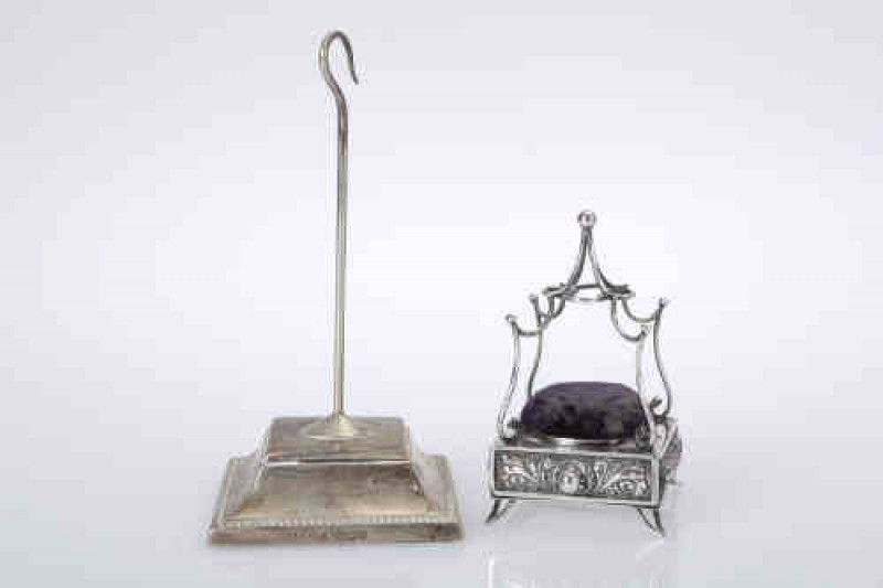 An Edwardian silver pin cushion, Birmingham 1904, the square platform with frieze drawer, chased to each side with anthemion and scrolls, raised on splayed feet; together with a silver dressing table stand. (2)