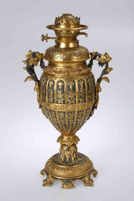 A Hinks & Sons gilt brass vasiform oil lamp, 19th century, the ovoid body issuing twin two-bar fruiting vine handles continuing to an acanthus leaf, cast in the round with stipple backed foliate panels, all above a collar cast with leaves within bell-shap