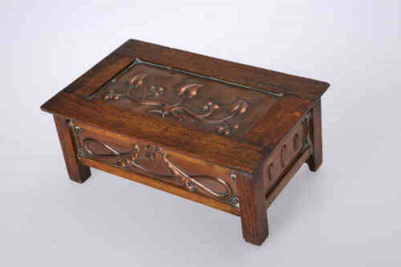 An Arts & Crafts copper and oak fall-front casket, the oak frame enclosing copper panels repousse with stylised platform, unmarked. 9.5cm by 24cm by 15cm