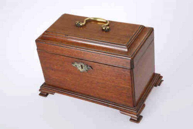 A George III mahogany tea caddy, with brass bail handle and cast brass foliate escutcheon, raised on ogee bracket feet. 20cm by 29cm by 17cm