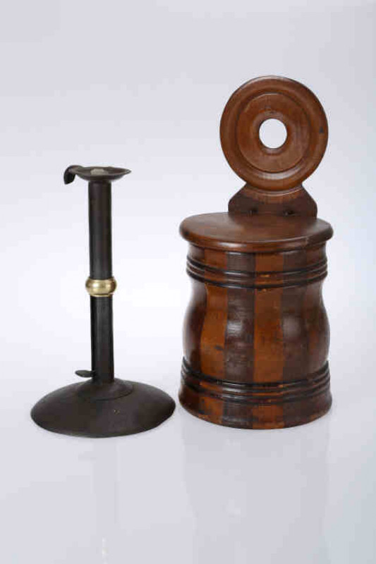 A Scottish staved treen salt barrel, 19th century, the hinged lid below a roundel with pierced hole for hanging; together with an iron ''hogscraper'' candlestick, with brass ''wedding band'', raised on a circular domed foot. (2) Candlestick 23cm