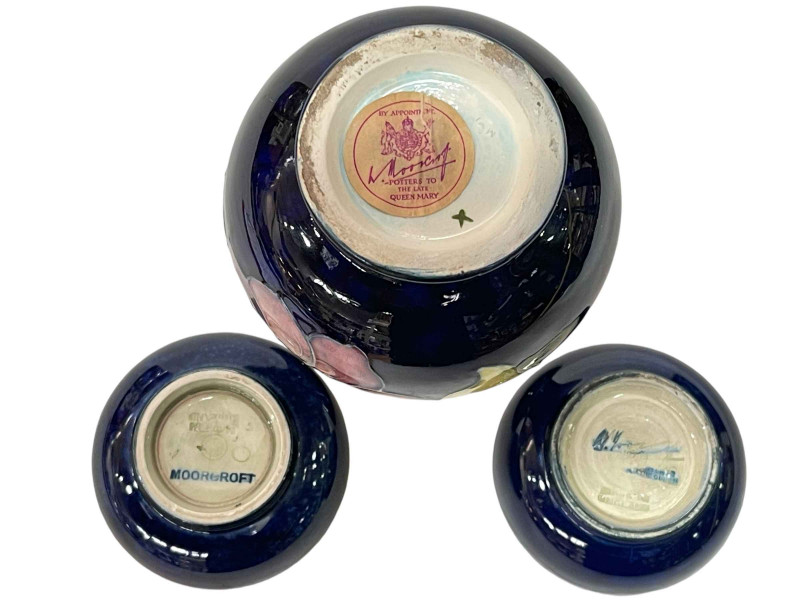 Two Moorcroft Pottery pin dishes decorated with orchid and pansy on blue ground, each 8cm in diameter, and Moorcroft Pottery baluster vase decorated with Clematis on blue ground, 13cm.