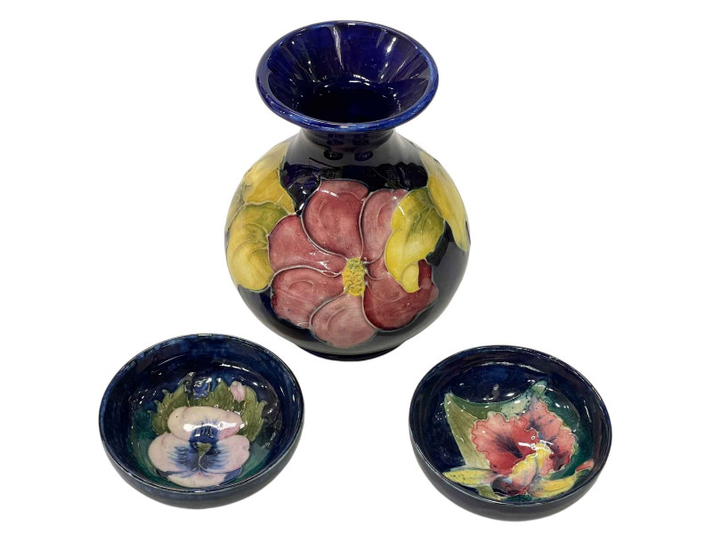 Two Moorcroft Pottery pin dishes decorated with orchid and pansy on blue ground, each 8cm in diameter, and Moorcroft Pottery baluster vase decorated with Clematis on blue ground, 13cm.