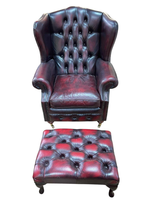 Ox blood buttoned leather and brass studded wing back armchair and footstool.