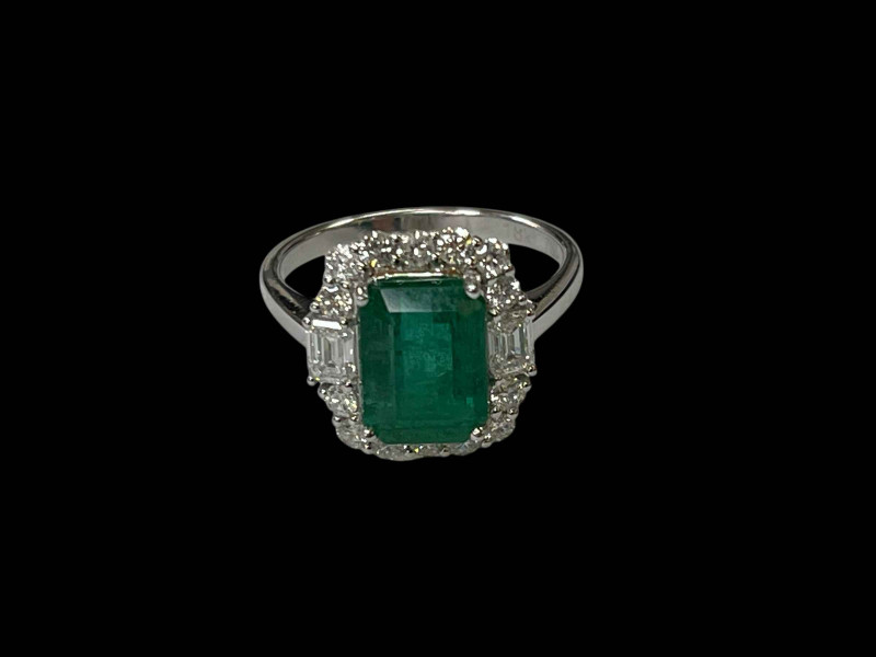 Emerald and diamond cluster ring set in 18 carat white gold, the rectangular 3 carat baguette cut emerald surrounded by fourteen round cut and two baguette diamonds totalling 0.90 carats, size O.