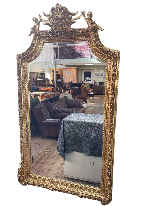 Rectangular gilt framed arched top bevelled wall mirror with shell and foliate crest supported by cherubs, 170cm by 99cm.