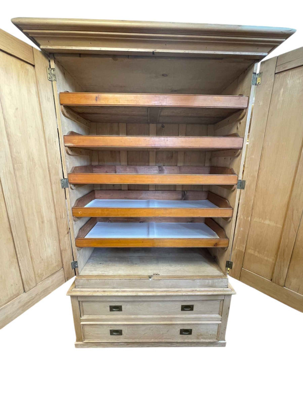 Victorian pine wardrobe having two doors enclosing five sliding trays above a base of two long drawers, 226cm by 141cm by 65cm.