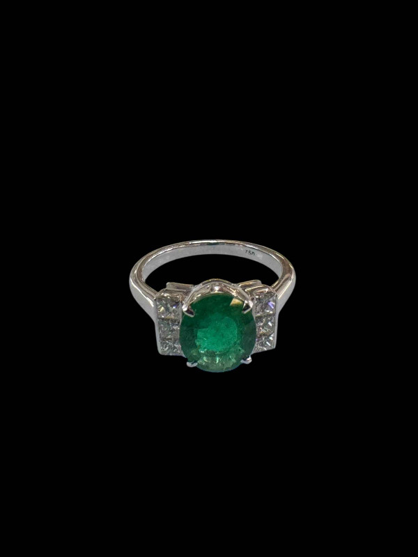 Emerald and diamond ring set in 18 carat white gold, the oval emerald 4.5 carats flanked by three princess cut diamonds to each shoulder, totalling 0.5 carats, size N.