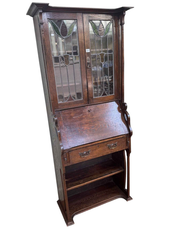 Art Nouveau oak bureau bookcase having two leaded glazed doors above a fall front with a drawer and shelf below, 181cm by 77cm by 38cm.