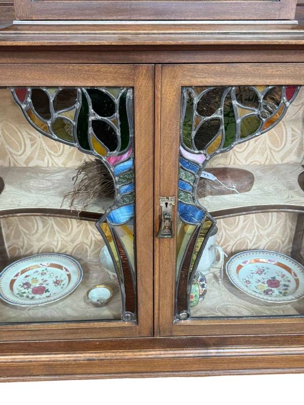 Art Nouveau mahogany cabinet, the canopied top having central glazed panel door flanked by two shaped shelves above two coloured leaded glass panel doors, 183.5cm by 138cm by 46cm.