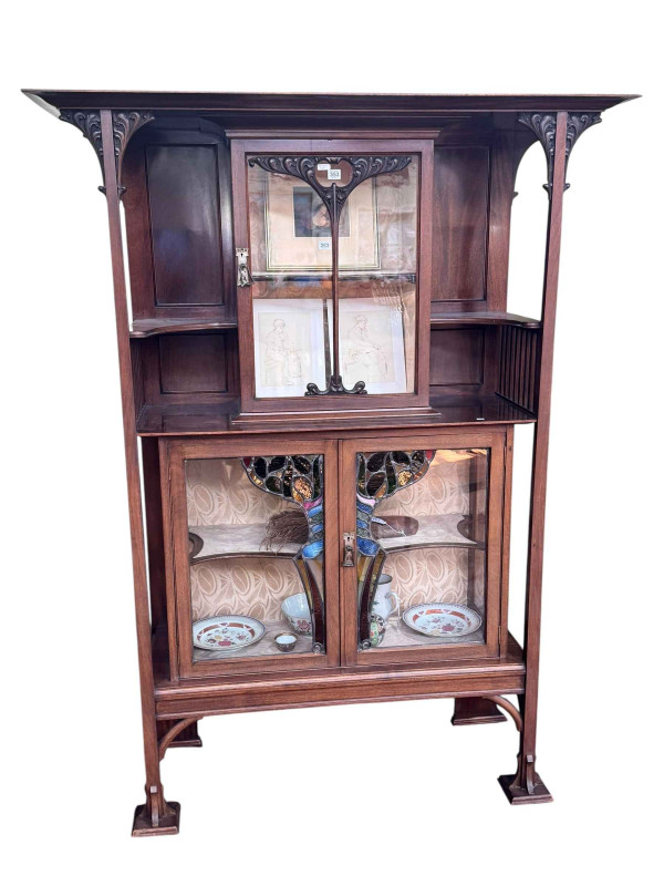 Art Nouveau mahogany cabinet, the canopied top having central glazed panel door flanked by two shaped shelves above two coloured leaded glass panel doors, 183.5cm by 138cm by 46cm.