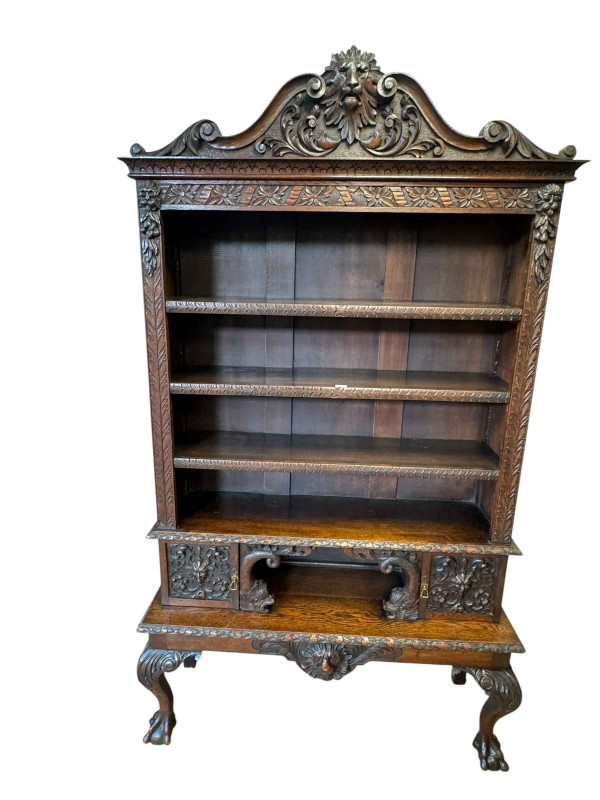 Victorian carved oak open bookcase having three adjustable shelves above an open compartment flanked by two carved cupboard doors on ball and claw legs, 202cm by 116cm by 38cm.