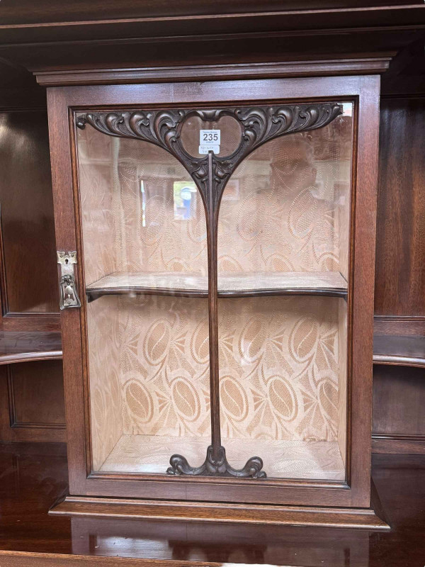 Art Nouveau mahogany cabinet, the canopied top having central glazed panel door flanked by two shaped shelves above two coloured leaded glass panel doors, 183.5cm by 138cm by 46cm.
