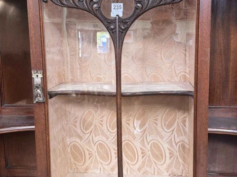 Art Nouveau mahogany cabinet, the canopied top having central glazed panel door flanked by two shaped shelves above two coloured leaded glass panel doors, 183.5cm by 138cm by 46cm. thumbnail