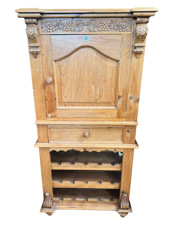 Pine wine cabinet having arched panelled door above a slide and drawer with a fifteen-bottle wine rack below, 142cm by 70cm by 47cm.