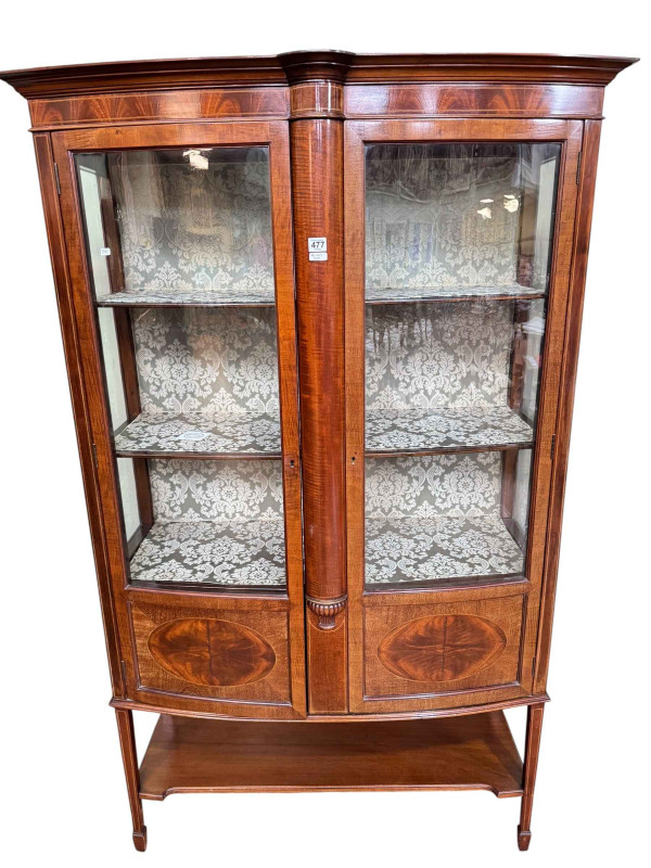 Edwardian mahogany shaped bow front two door vitrine having undershelf on square tapering legs to spade feet, 175cm by 108cm by 47cm.