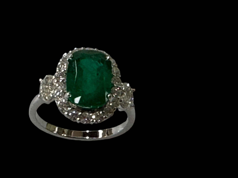 Impressive emerald and diamond cluster 18 carat white gold ring, the cushion emerald bordered with eighteen diamonds and the shoulders each having an oval diamond, size N.