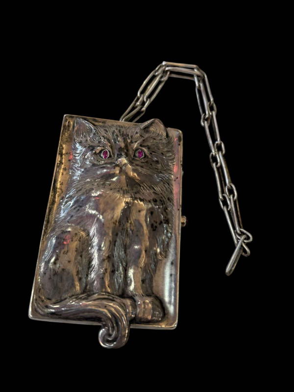 Louis Kuppenheim silver vanity case, the front and back with repousse cat having ruby eyes, fitted interior with cabachon ruby openers, with chain, 10.5cm by 6cm.