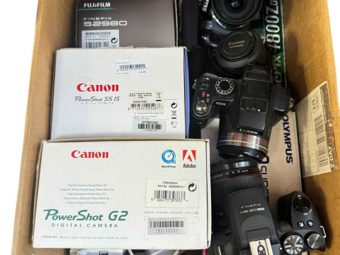 Box of digital cameras including Canon IXS 185, Panasonic G5, etc.
