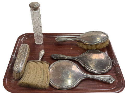 Two silver backed mirrors, three silver brushes and silver topped bottle.