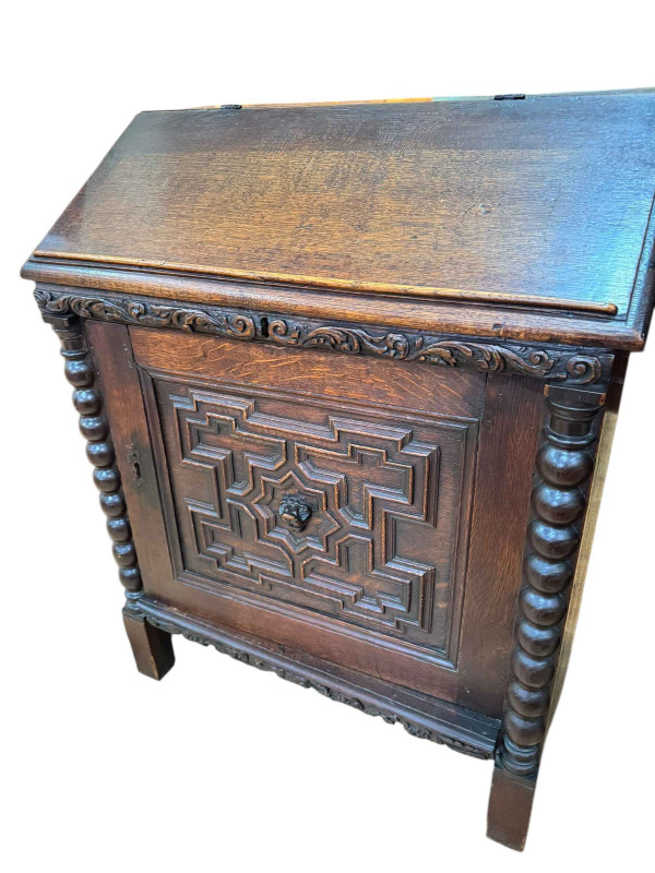 19th Century carved oak desk, the slope top front enclosing eight drawers with a carved panel cupboard door below, 101cm by 82cm by 49cm.