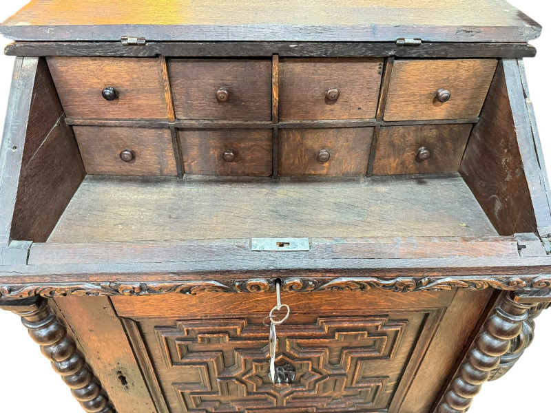 19th Century carved oak desk, the slope top front enclosing eight drawers with a carved panel cupboard door below, 101cm by 82cm by 49cm.