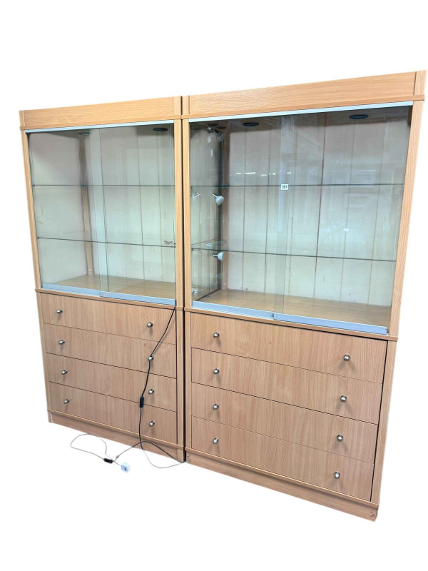 Pair beech finish illuminated shop display cabinets having two sliding glazed doors above four drawers, 191cm by 99.5cm by 49.5cm.