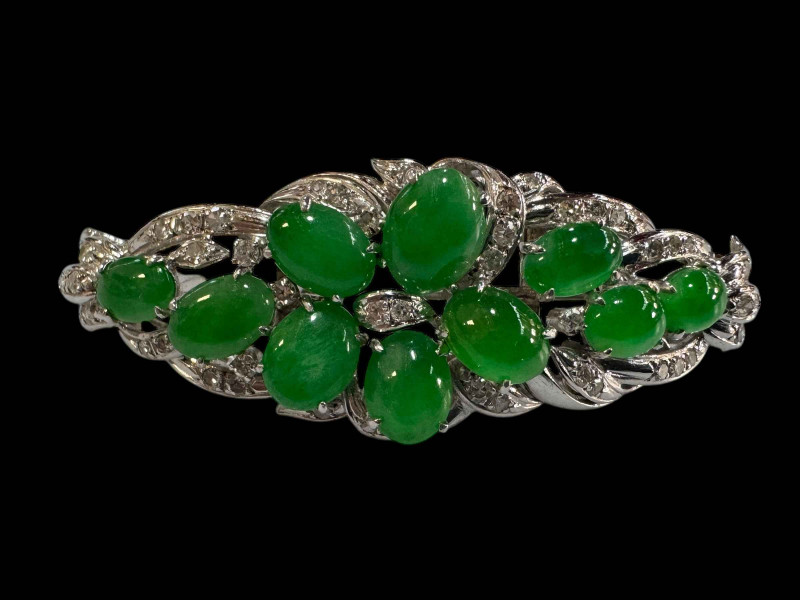 An 18 carat white gold, green jade and diamond set brooch/pendant set with ten cabachon jade stones and round cut diamonds.