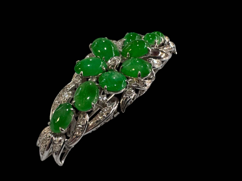 An 18 carat white gold, green jade and diamond set brooch/pendant set with ten cabachon jade stones and round cut diamonds.