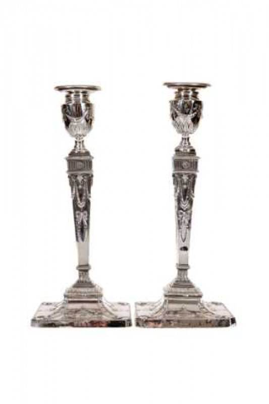 A handsome pair of Adam Revival silver candlesticks, Greenberg & Co, Birmingham 1906 and 1908, embossed with ribbon tied floral swags and rams heads, raised on square bases decorated with urns and acanthus leaves, weighted. 30cm