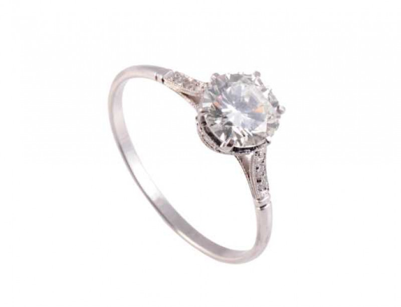 A diamond ring, the central six claw set brilliant cut diamond set in a pierced detail textured mount above a surround of ten brilliant cut diamond highlights to the centre of the mount, all between open shoulders with similar textured detailing, set with