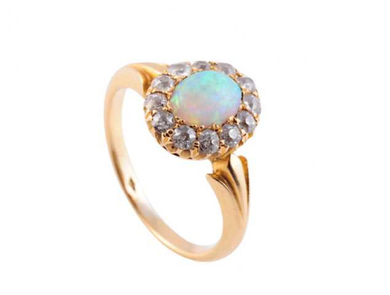 An opal and diamond ring, the central oval cut opal claw set within a bezel of twelve old brilliant cut claw set diamonds, all set in a pierced detail mount between tapering leaf shaped shoulders on a plain band. Ring size L1/2