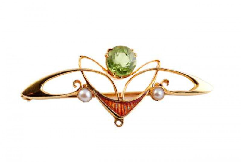 An Art Nouveau peridot, seed pearl and enamel brooch, set with a round cut three double claw set peridot to the top of a swirling symmetrical abstract design of knife edge bars, the bottom set with a plaque of red enamel between a collet set seed pearl hi