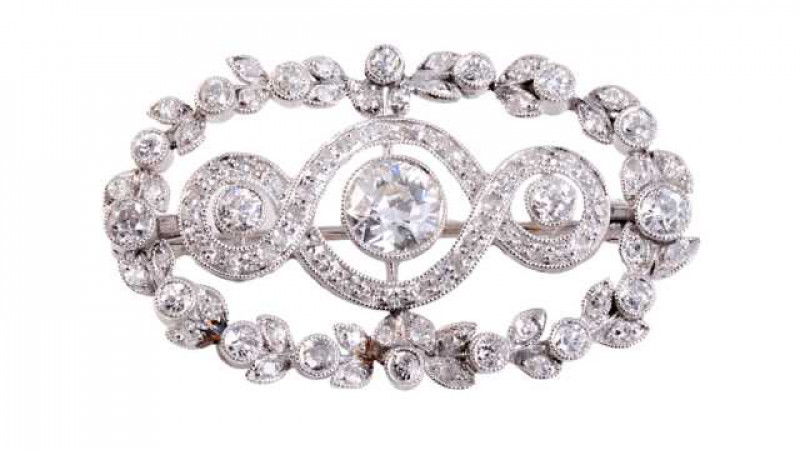 An elegant Edwardian diamond brooch, set to the centre with a round mixed cut millegrain set diamond and two smaller round mixed cut millegrain set diamonds set within an inner coil, the entirety set with round mixed cut diamond highlights, all set within