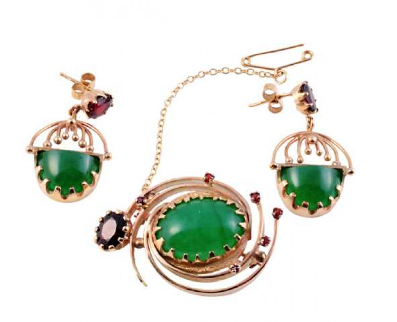 A jadeite and garnet brooch and pair of earrings, the brooch set to the centre with a claw set oval cabochon cut jadeite within a swirl designed mount of four delicate strands, set throughout with six claw set round cut garnet highlights, all set to the b
