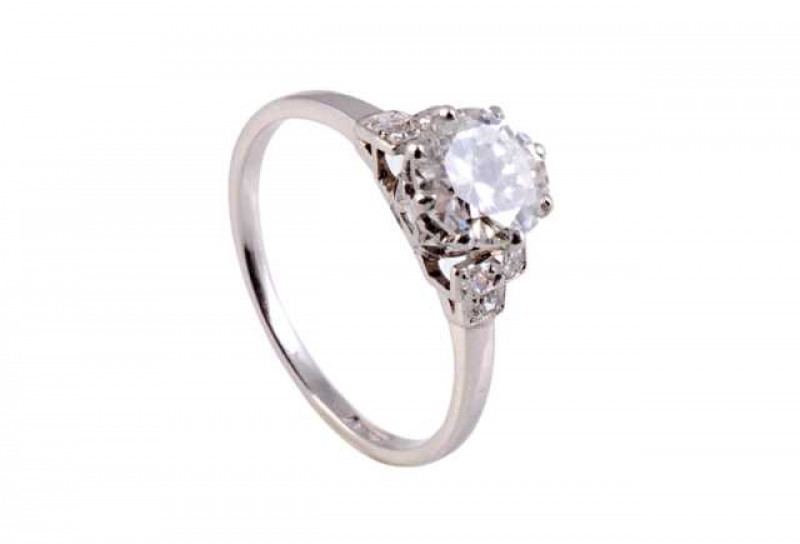 A diamond ring, the central brilliant cut diamond eight claw set in a pierced detail mount, between stepped slightly tapering shoulders set with three brilliant cut claw set diamond highlights, on a plain band. Stamped PLAT. Size M1/2