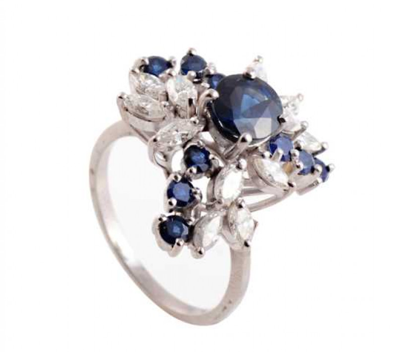 A sapphire and diamond ring, the circular mixed cut four claw set sapphire set high within a stylised three sectioned leaf shaped mount, each section set with three circular mixed cut claw set sapphires and four marquise cut claw set diamonds, all set on 