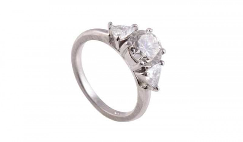 A three stone diamond ring, the central brilliant cut four claw set diamond set between two trillion cut three claw set diamonds, all set in an open mount between plain shoulders on a plain band. Stamped 950. Ring size K1/2