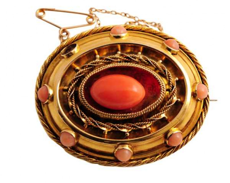 A mid Victorian coral brooch, set to the centre with an oval shaped coral bead, within a concave mount set with rope work detailing, in turn within a mount set to the edge with evenly spaced collet set coral beads (one lacking), within a border of similar