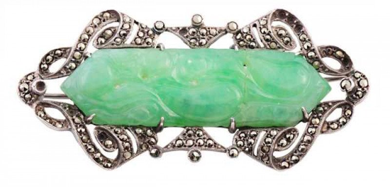 A green stone and marcasite brooch, the carved and pierced detailed green stone plaque eight claw set within a scrolling detailed mount set throughout with marcasite highlights (some lacking). Stamped SILVER. Weight approx. 12.4gms. Length approx. 5cm.
