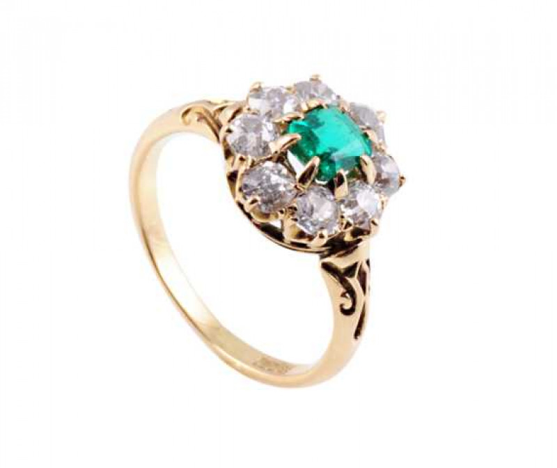 An emerald and diamond ring, the square cut emerald eight claw set within a bezel of eight old brilliant cut claw set diamonds, all set in a pierced detail and open mount between moulded detail shoulders on a plain band. Stamped 18CT. Ring size N.