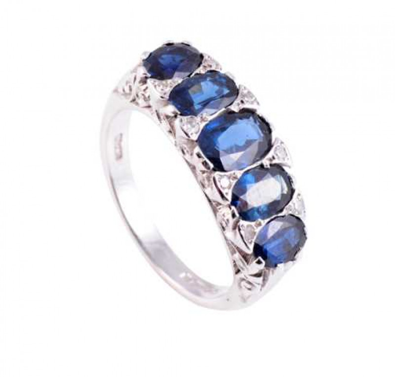 A sapphire and diamond ring, the five oval cut graduating sapphires and eight diamond highlights set in a pierced detail and open mount, between moulded tapering shoulders on a plain band. Stamped 750. Ring size O.