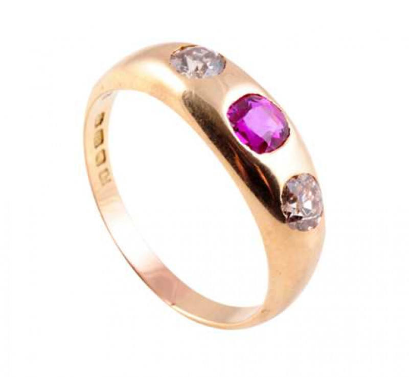 A diamond and ruby ring, the round mixed cut ruby collet set between a round mixed cut collet set diamond to each side, all evenly spaced, set in a plain wide mount between slightly tapering shoulders on a plain. Stamped 18. Ring size R.