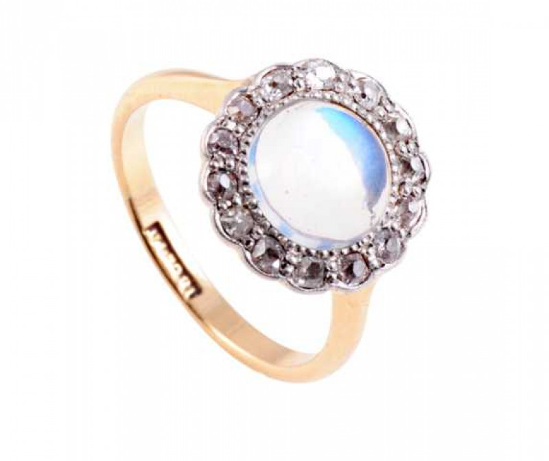 A moonstone and diamond ring, the round cabochon cut moonstone set within a bezel of fourteen rose cut diamonds in a moulded mount, all set in a pierced detail mount between plain shoulders on a plain band. Stamped 18CT PT. Stamped K1/2