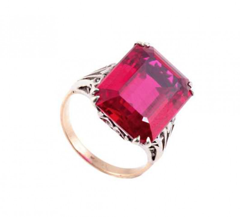 A red stone ring, the large rectangular cut red stone four double claw set in an open and elaborately pierced detailed mount, between tapering open shoulders with similar pierced design detailing, on a plain band. Ring size J.