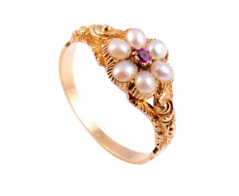 A garnet and seed pearl ring, circa 1840-1850, the table cut ruby highlight eight claw set within a surround of six seed pearls, all set in a moulded shaped mount with circular glass hair locket underneath, between elaborately moulded shoulders with chase