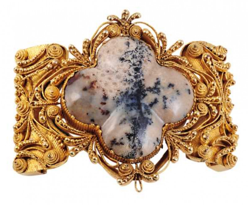 A hardstone brooch, circa 1800, the fancy cut moss agate collet set within a curved symmetrical elaborately detailed moulded mount of chased and beaded detailing, texturing and delicate scroll work. Engraved to the back of the mount 'Betsy Larkin Died Apr
