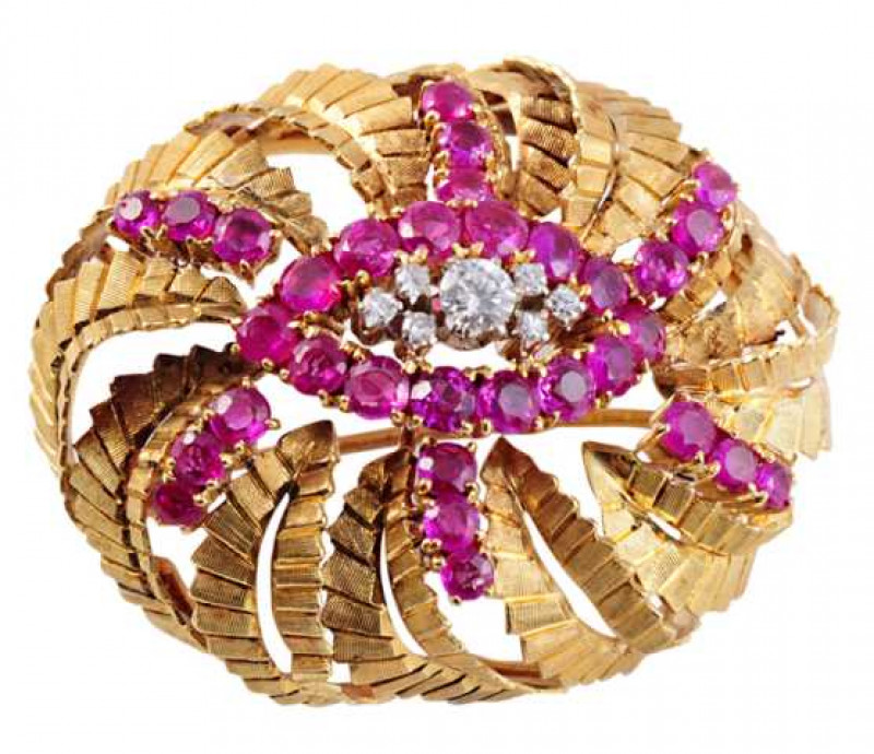 A ruby and diamond brooch, the domed mount set to the top with a brilliant cut six claw set diamond between a cluster of three smaller brilliant cut claw set diamonds to each side, all set within a surround of fourteen round cut claw set rubies with a fur